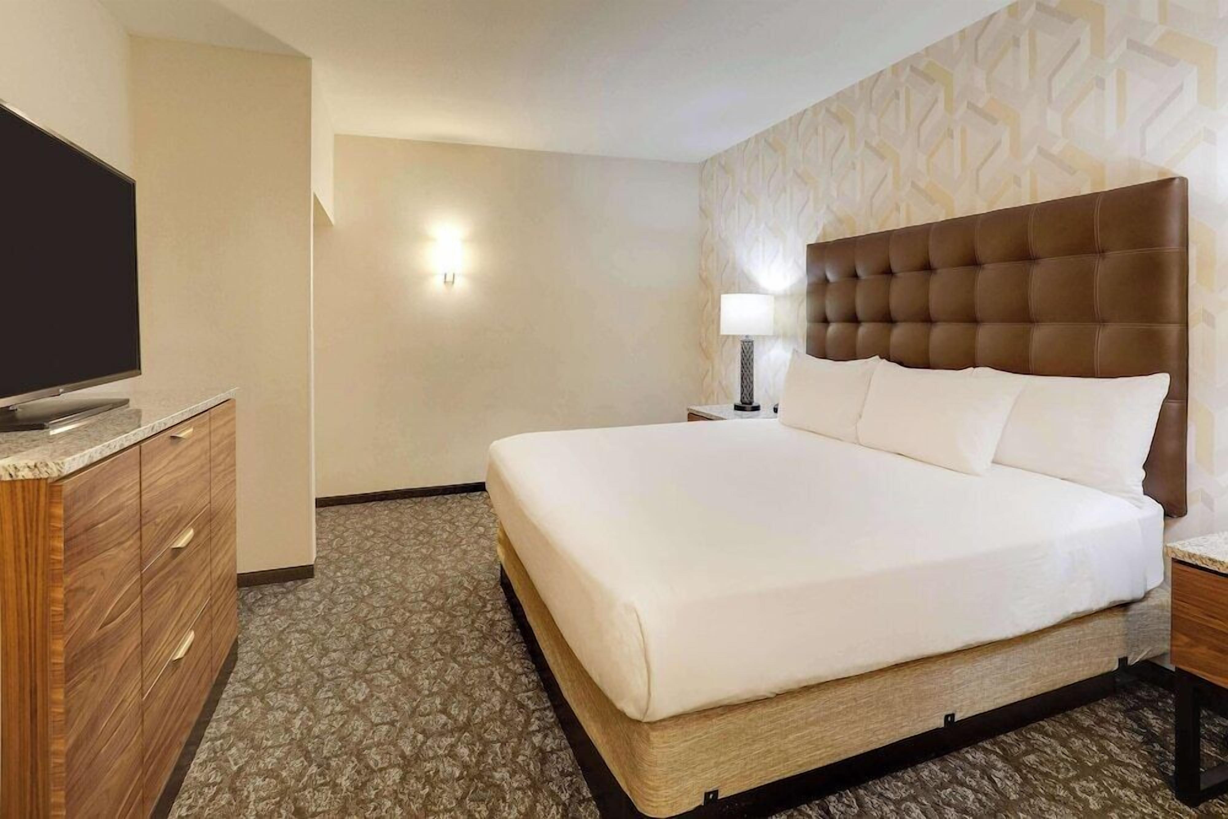 Quarto de hotel com uma cama grande, televisão sobre um móvel de madeira e parede estampada.