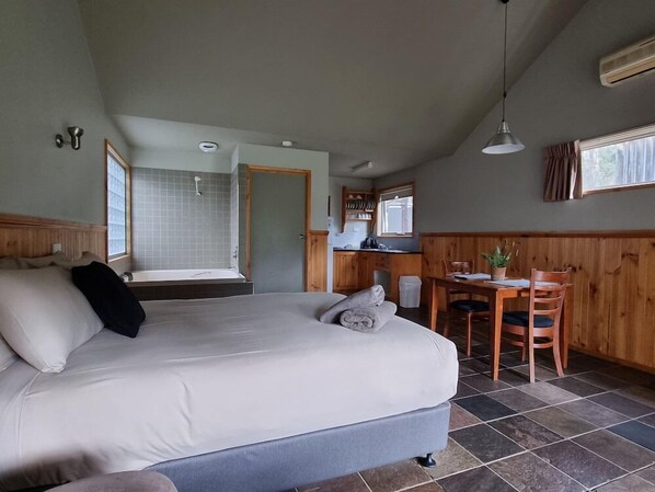 Un dormitorio con una cama grande, un baño con ducha y una pequeña zona de comedor con mesa y sillas.