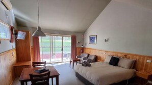 Quarto de hotel com cama, escrivaninha, duas cadeiras, mesa, abajur e vista para o exterior.