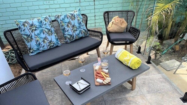 An outdoor seating area with a sofa, two chairs, a table with food and drinks, and a yellow towel. - Mulwala Murray River Motel (Mulwala)