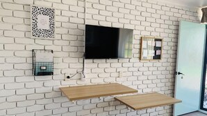 A room with a white brick wall, a flat-screen TV mounted above a wooden shelf, a door with a key in the lock, and a small framed picture on the wall. - Mulwala Murray River Motel (Mulwala)