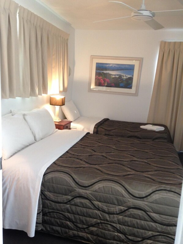 Een hotelkamer met een bed, nachtkastje, lamp, plafondventilator en een ingelijst schilderij aan de muur.