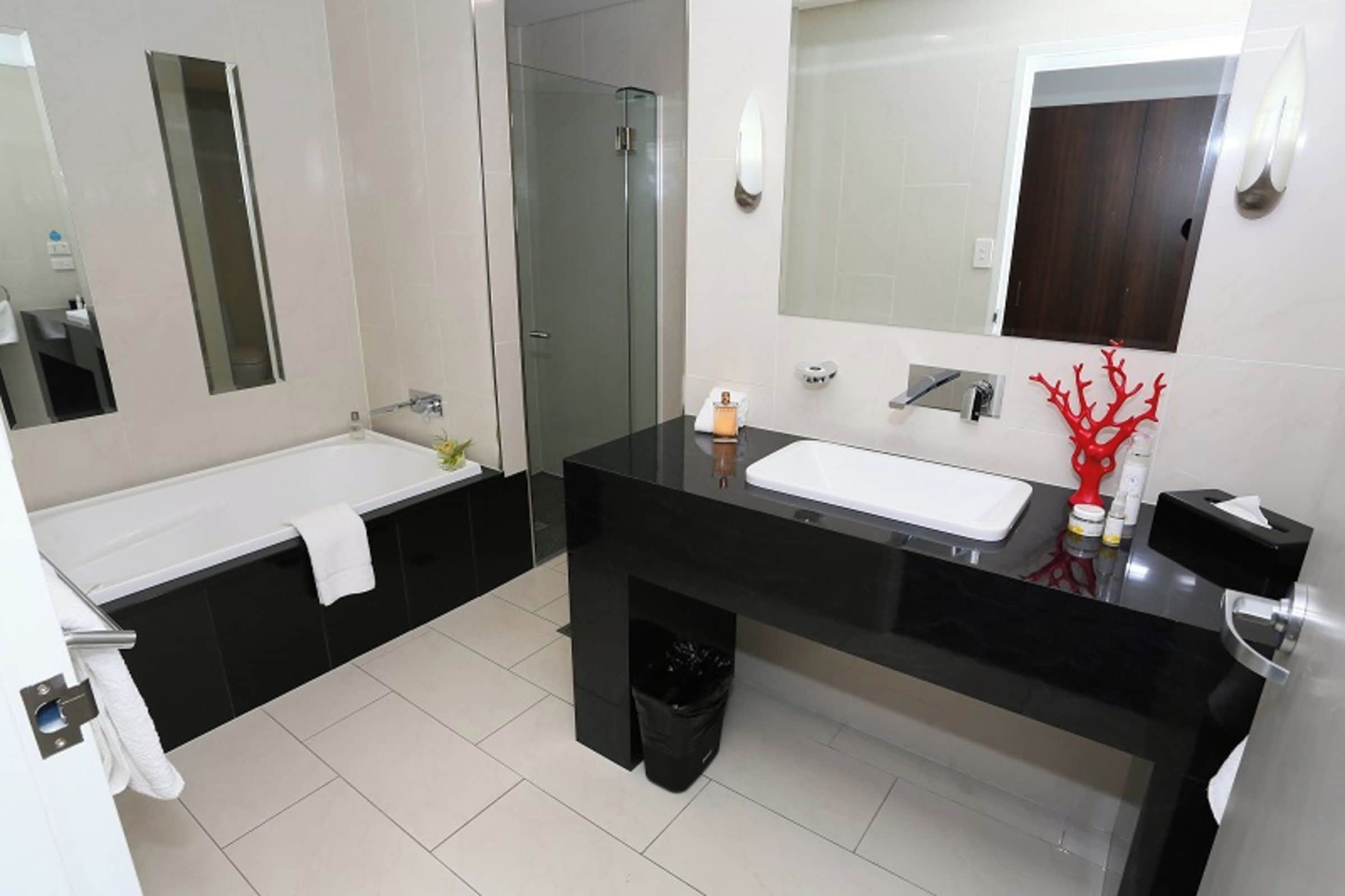 Un baño moderno con encimera negra, lavabo blanco y cabina de ducha con mampara de vidrio.
