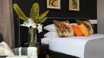 A hotel room with a bed, white pillows, a nightstand, a vase with flowers, and two framed pictures on the wall.