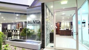 Restaurante en BLVD con zona de recepción, mesas dentro y una pequeña fuente de agua afuera.