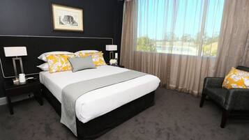 A hotel room with a large bed, two bedside tables, a chair, a window with curtains, and a framed picture on the wall.