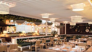 Un restaurant doté d’une grande salle à manger commune, de tables individuelles, de jardinières suspendues et de luminaires suspendus.