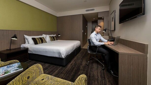 Une chambre d’hôtel comprenant un lit, un bureau avec un ordinateur portable, une chaise, une télévision et une table de chevet avec une lampe.