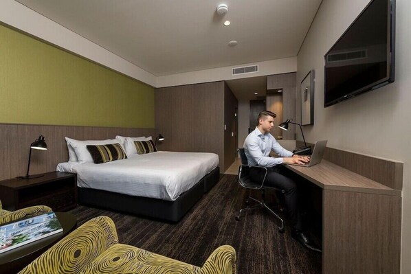 Une chambre d’hôtel comprenant un lit, un bureau avec un ordinateur portable, une chaise, une télévision et une table de chevet avec une lampe.