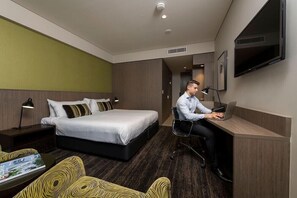 Een hotelkamer met een bed, een bureau met een laptop, een stoel, een televisie en een nachtkastje met een lamp.