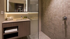 Une salle de bain moderne avec une douche à l’italienne en verre, un meuble-lavabo avec un miroir et un mur de douche carrelé.
