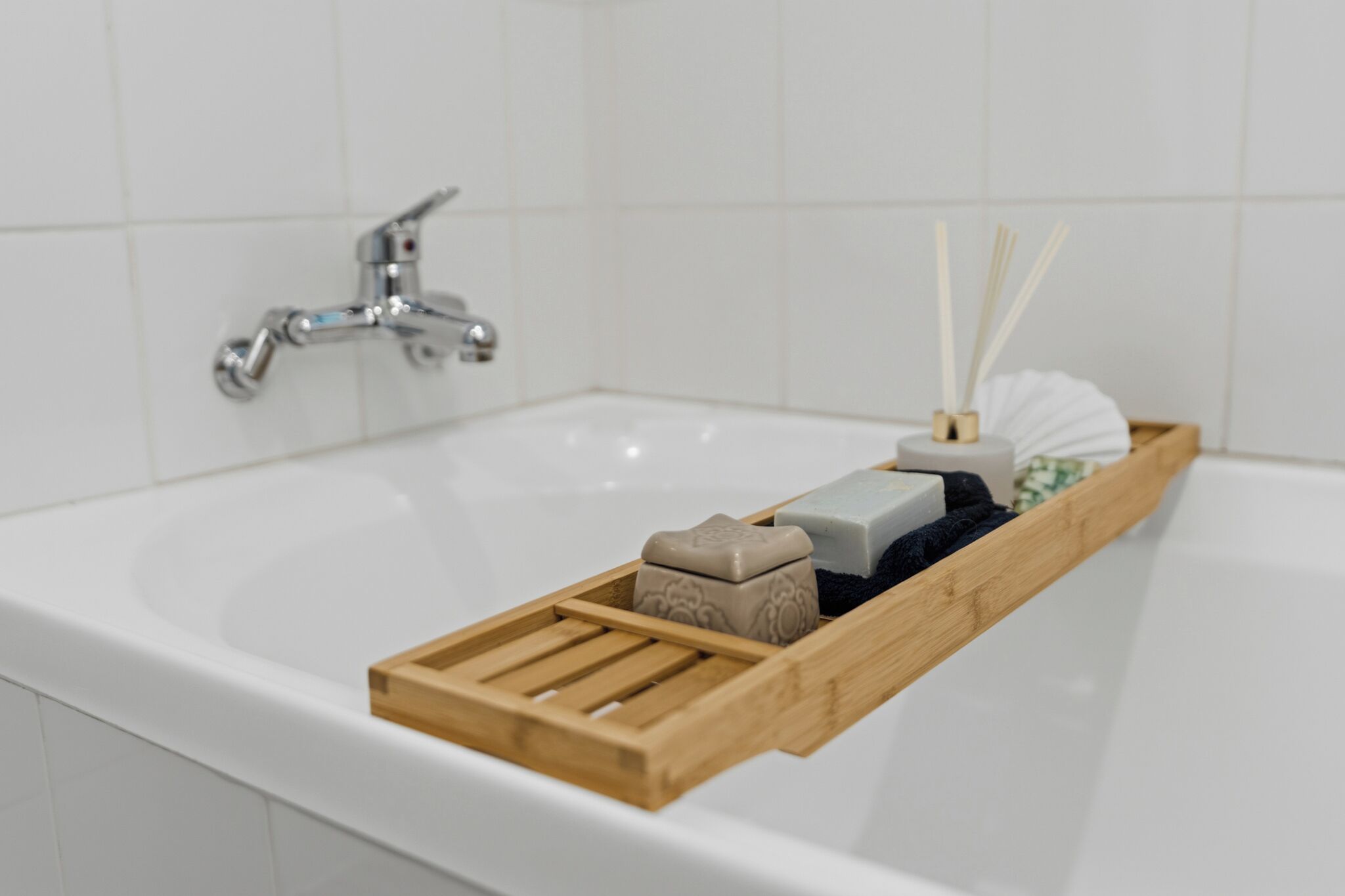 Un baño con una bañera blanca, una bandeja de madera con artículos de aseo y una pared de azulejos blancos.