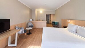 A hotel room with a bed, a TV, a desk, a chair, a small table, and a microwave. - El Toro Motor Inn (Sydney)