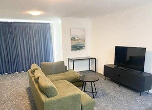 A living room with a sofa, a small table, a TV, and a painting on the wall. - El Toro Motor Inn (Sydney)