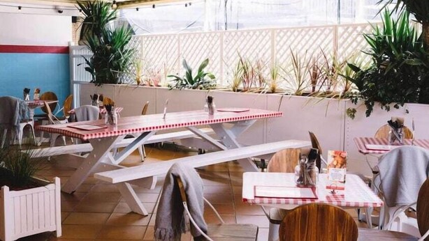 An outdoor patio area with tables and chairs, surrounded by plants and a white fence. - El Toro Motor Inn (Sydney)