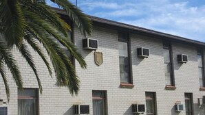 A building with a brick facade, multiple air conditioning units, and a shield emblem on the wall. - El Toro Motor Inn (Sydney)