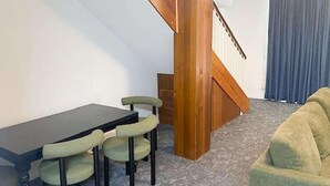 A room with a dining table, chairs, a sofa, a wooden staircase, and a window with curtains. - El Toro Motor Inn (Sydney)