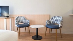 A hotel room with two patterned chairs, a small round table, and a television on a stand. - El Toro Motor Inn (Sydney)