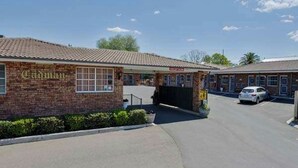 A brick building with a tiled roof, a covered entrance, and a parking area with a car. - Cadman Motor Inn Tamworth (Tamworth)