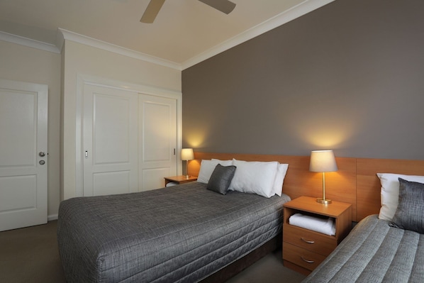 A hotel room with two beds, a wooden headboard, bedside tables with lamps, and a door. - Cadman Motor Inn Tamworth (Tamworth)