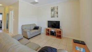 A living room with a sofa, a television on a stand, and a tiled floor. - Cadman Motor Inn Tamworth (Tamworth)