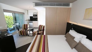 A modern hotel room with a large bed, a desk, a chair, and a view of the outdoors. - Seahaven Resort (Sunshine Coast)
