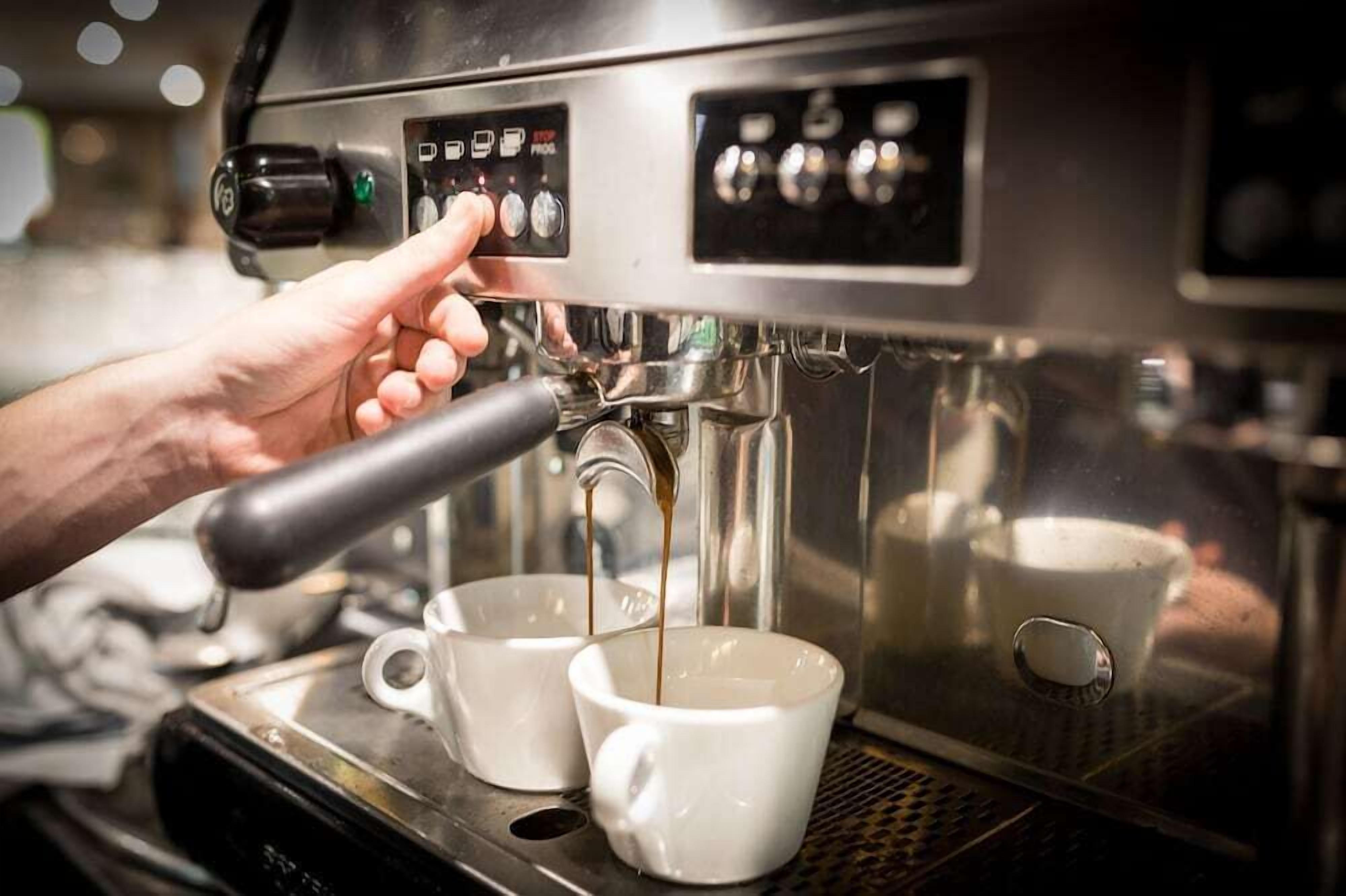 Una mano ajustando una máquina de café espresso, con dos tazas debajo.