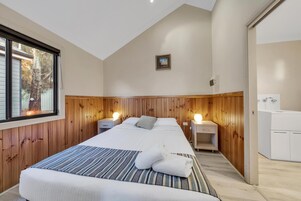 Quarto com cama grande, duas mesas de cabeceira, guarda-roupa e janela com vista para árvores.