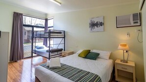 Una habitación con una cama individual, una litera, una mesita de noche con lámpara, un cuadro en la pared y una ventana con cortinas.
