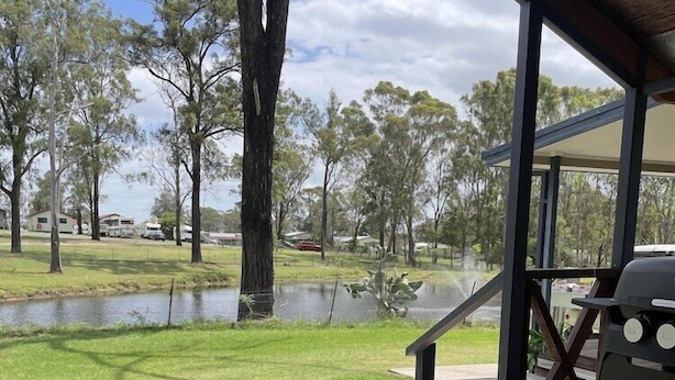 Un espacio al aire libre techado con una parrilla y vistas a un campo cubierto de césped y árboles.