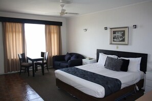 A hotel room with a large bed, a desk with two chairs, a sofa, and a ceiling fan. - Lakeview Motel & Apartments (Robe)