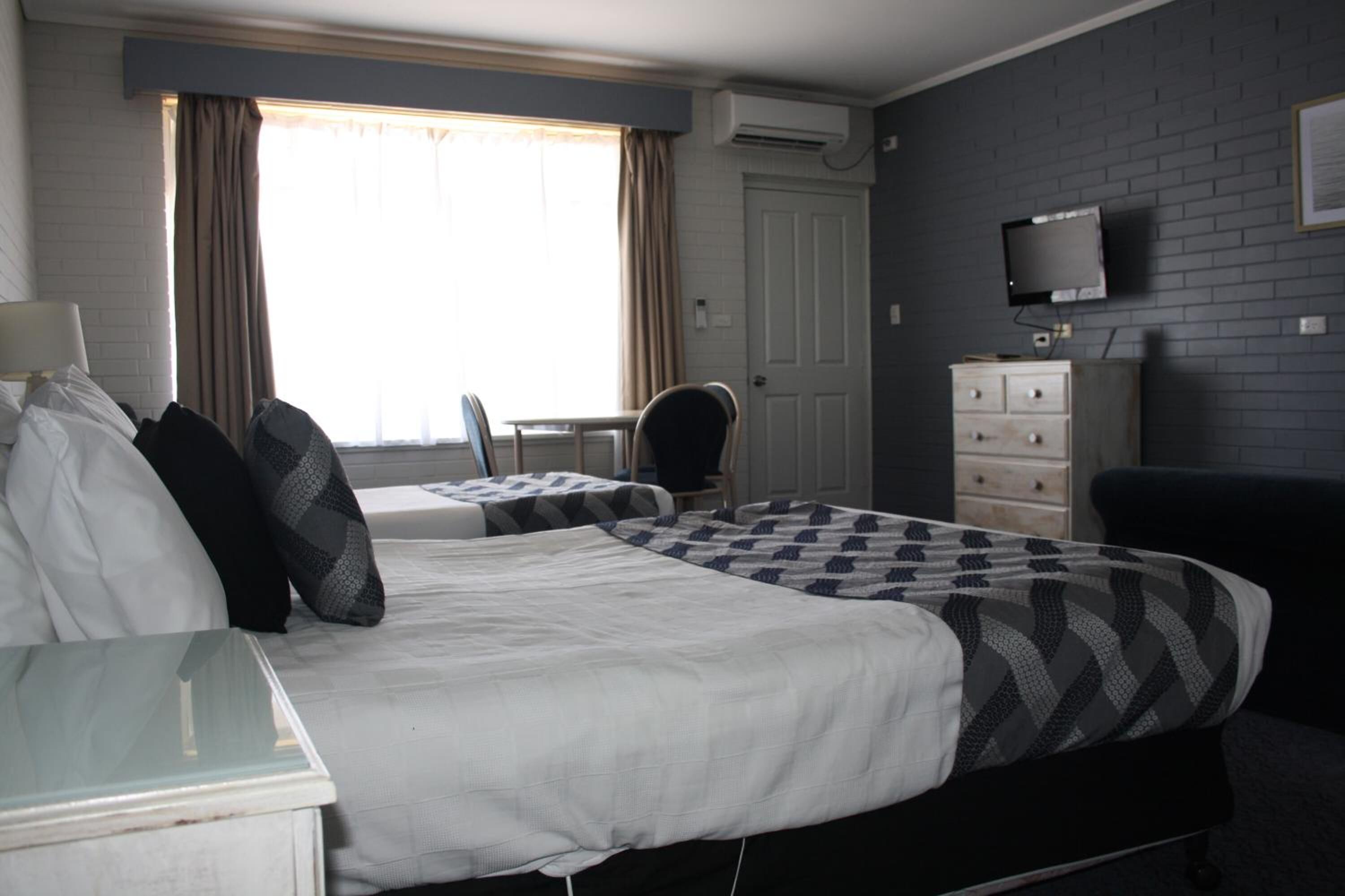 Una habitación de hotel con una cama, un escritorio, una silla, un aparador y un televisor en la pared.