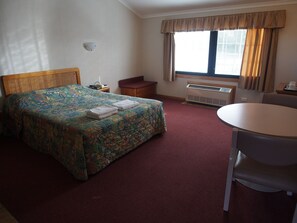 Ett hotellrum med en säng, ett skrivbord, en stol, en värmare och ett fönster med gardiner.
