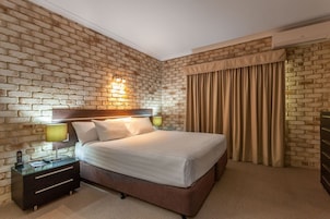 Habitación de hotel con pared de ladrillo, cama con ropa blanca, mesita de noche con lámpara y un armario.