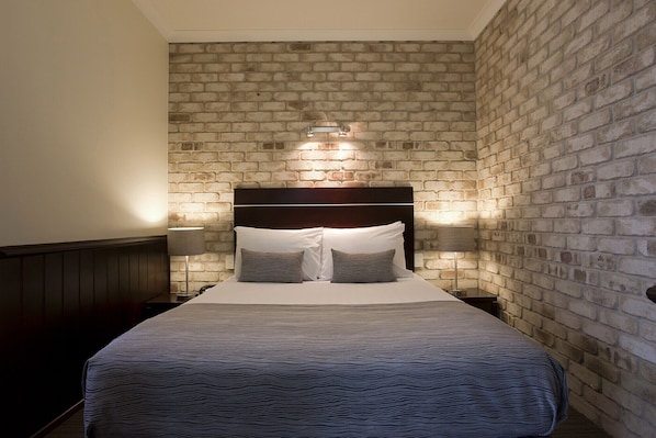A bedroom with a brick-patterned wall, a dark headboard, and two bedside lamps. - Highlander Motor Inn (Toowoomba)
