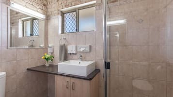 A bathroom with a sink, mirror, towel rack, and a glass shower enclosure.