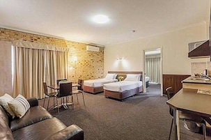 Habitación de hotel con pared de ladrillo decorativa, un sofá, dos camas, un escritorio y un comedor.