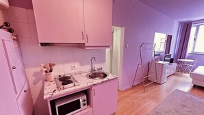 Et lille køkken med vask, mikroovn og kogeplade. Der er et spiseområde med et bord og stole.