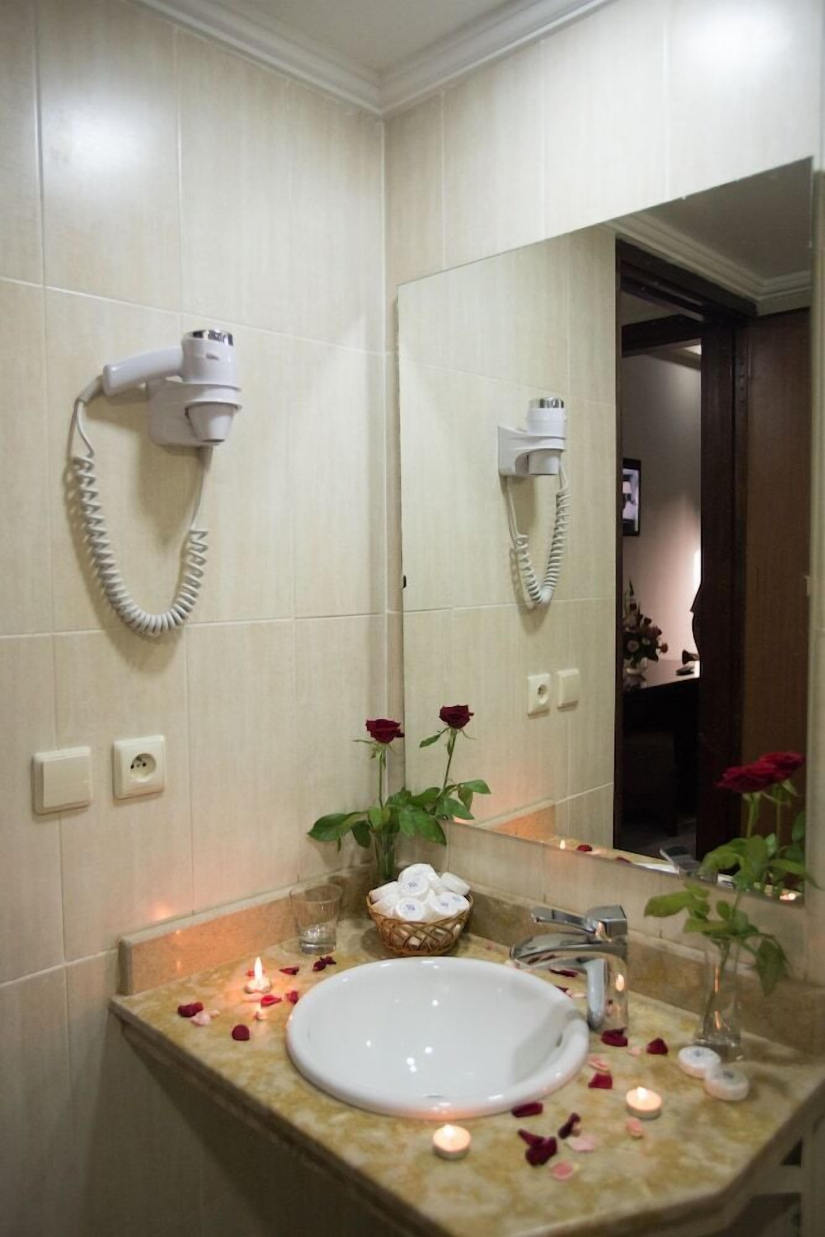 A bathroom with a sink, mirror, hairdryer, and a small basket of toiletries.