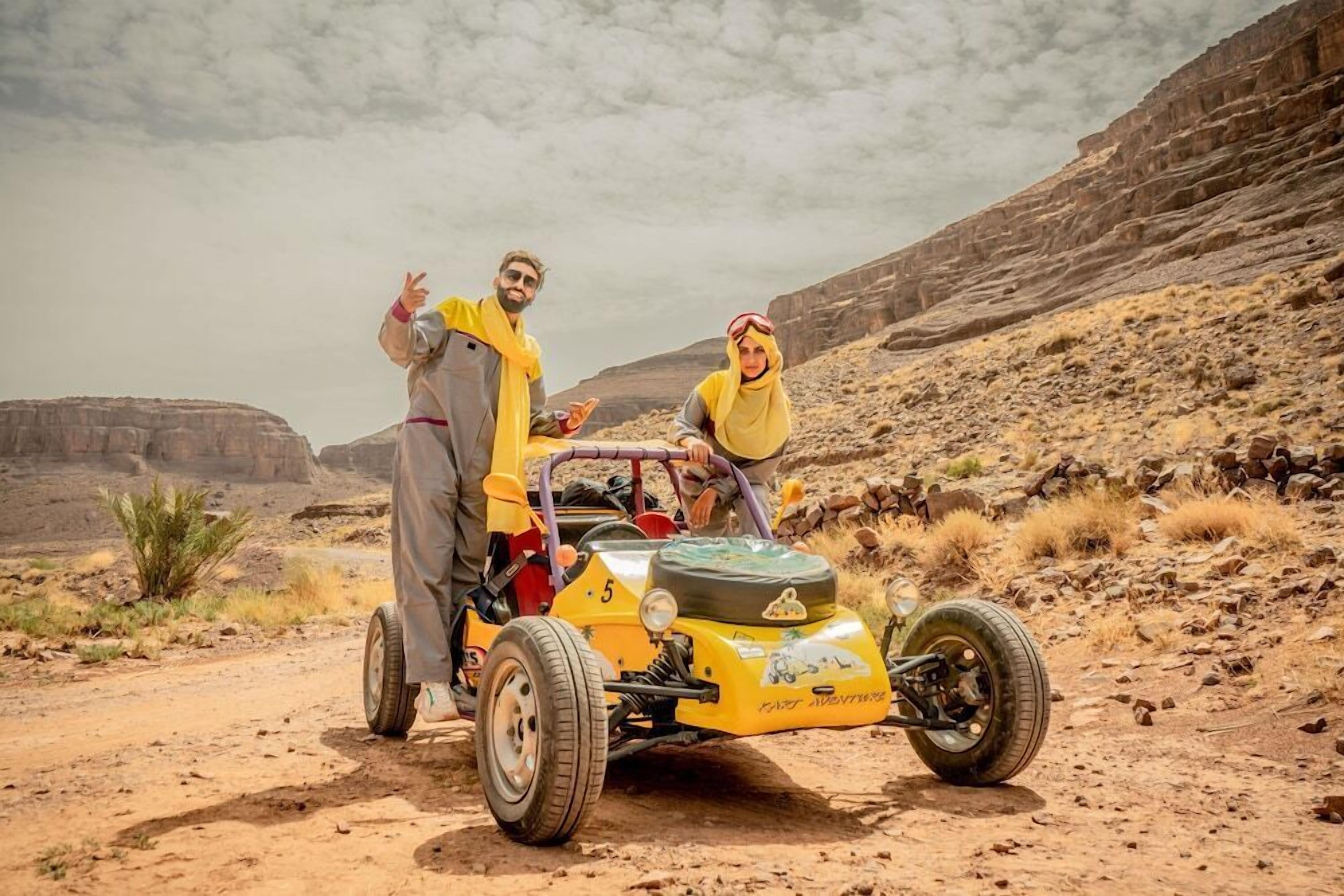 A desert landscape with a yellow off-road vehicle and two people.