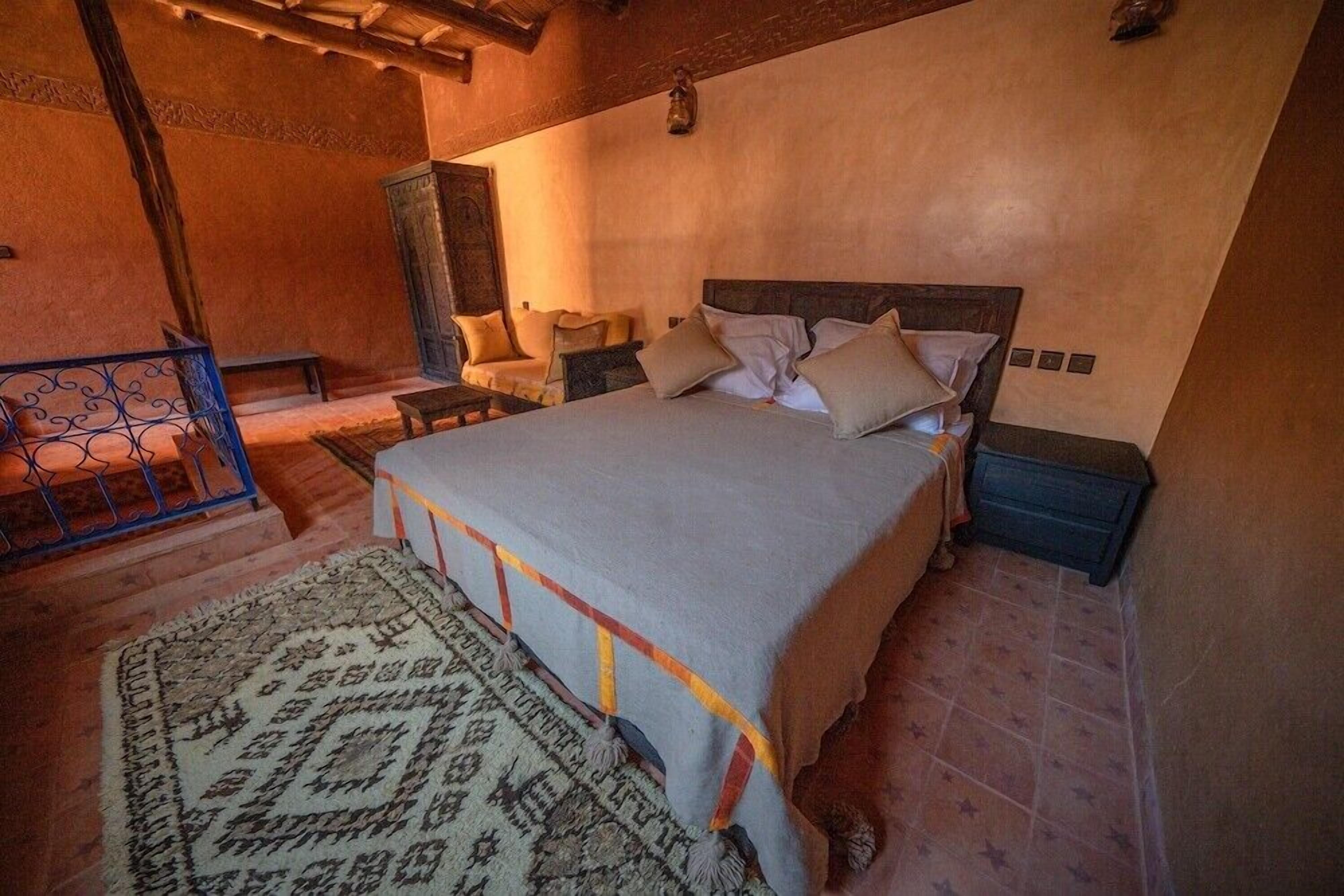 A bedroom with a bed, nightstands, a chair, a wooden cabinet, and a patterned rug.