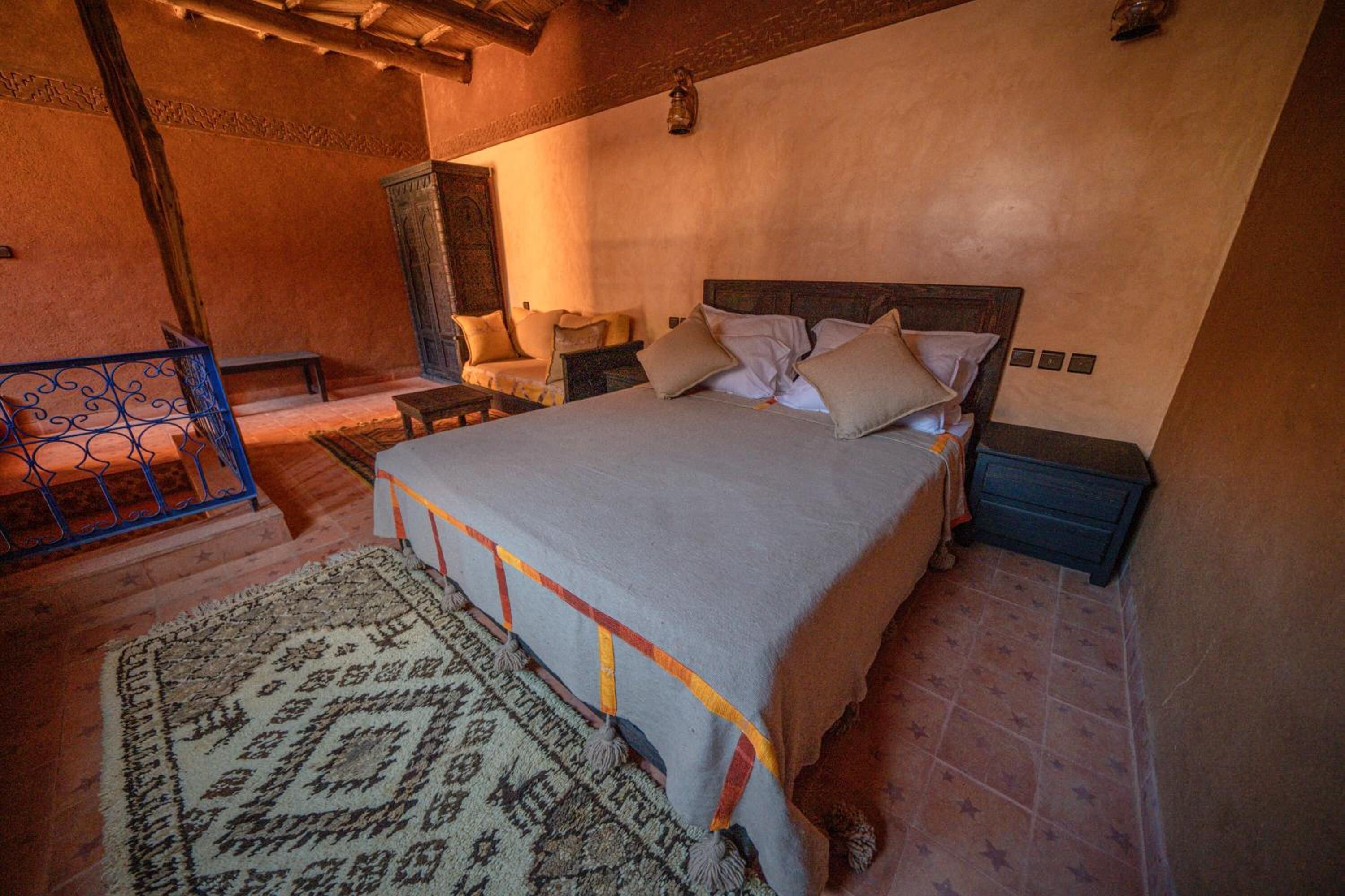 A bedroom with a large bed, a nightstand, a wooden cabinet, a bench, and a patterned rug.