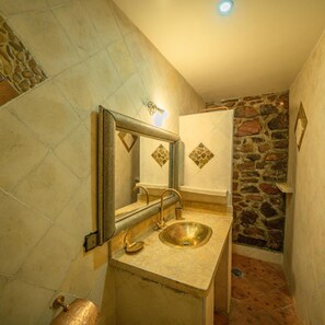 Un baño con pared de piedra, un lavamanos con lavabo dorado y un espejo con marco decorativo.