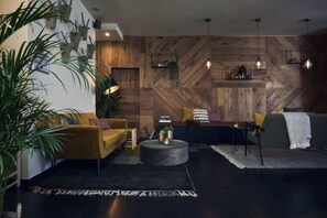 A modern living room with a herringbone wood wall, a yellow sofa, a round coffee table, and pendant lighting. - Best Western Plus Hotel Atlant (Genk)