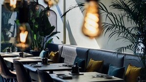 A modern dining area with a long table, cushioned seating, hanging light fixtures, and large windows. - Best Western Plus Hotel Atlant (Genk)