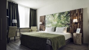 A hotel room with a large bed, a chair, a desk, and a view of trees through the window. - Best Western Plus Hotel Atlant (Genk)