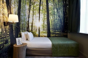 Un dormitorio con una cama, una lámpara de noche, una cita enmarcada y un mural de un bosque en la pared.