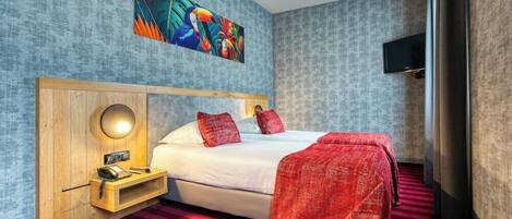 Habitación de hotel con cama, mesita de noche con lámpara, un cuadro en la pared y televisión también en la pared.