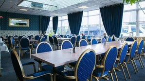 A conference room with multiple tables and chairs, large windows with curtains, and a ceiling with a skylight.