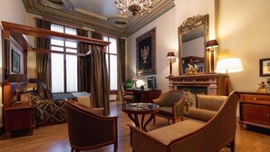 A spacious room with a large bed, a sitting area with a fireplace, a desk, and a television. - Grand Hotel De Draak And Residence Dagmara (Bergen op Zoom)